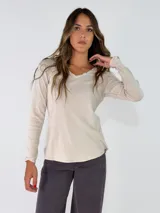 Remera de manga larga en color beige, con escote en V y detalle de terminación desflecada en el borde del cuello.