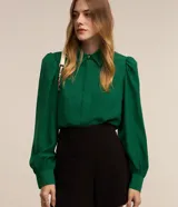 Camisa de crepé color blanco, con cuello inglés, manga larga abullonada con puños abotonados y cierre frontal oculto con botón diferenciado en el cuello.