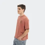 Remera oversize color terracota con efecto acid wash y estampa circular en el pecho. Presenta cuello redondo y terminaciones sin dobladillo en mangas y ruedo.