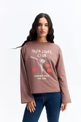 Remera de manga larga color marrón con estampa frontal con la frase 'Pasta Lover Club' y dibujos de un tenedor con pasta y tomates. Presenta un corte holgado y cuello redondo.