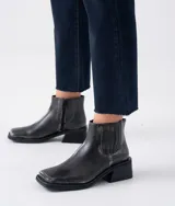 Bota corta tipo chelsea de cuero vacuno color negro, con puntera cuadrada, taco cuadrado de madera y detalle de textura grabada en el panel elástico lateral.