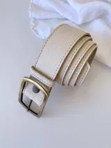 Cinto de cuero texturizado en color crudo, con hebilla metálica rectangular de acabado envejecido y sistema de broche suizo intercambiable.