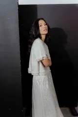 Blusa color crudo de lino con mangas cortas y detalle de flecos en el ruedo y las mangas. Cierre con botón en la espalda.