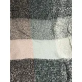 Bufanda rectangular de tejido grueso con diseño de cuadros en tonos azul, naranja, gris y beige, terminada con flecos en los extremos.