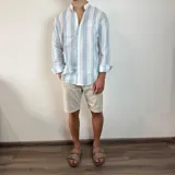 Camisa celeste y blanca a rayas verticales, de lino, con cuello mao y mangas largas con puños.