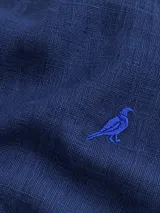 Camisa de lino color blanco, manga larga, con cuello corto clásico y bordado de un ave oscura en el pecho.