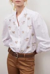 Camisa blanca de manga corta con cuello mao y volados, botones frontales y bordados de hojas y flores en color dorado.