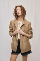 Blazer de silueta amplia y largo por debajo de la cadera, color café, confeccionado en tela suave y liviana. Presenta cuello con solapas, cierre cruzado con botones y bolsillos laterales con tapa.