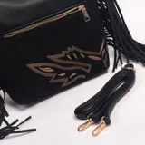 Cartera tipo hobo de color negro, confeccionada en cuero sintético, con detalles de flecos en los laterales, herrajes dorados y un diseño bordado en hilo dorado en la parte inferior. Incluye asa corta de hombro y correa extraíble regulable.