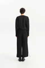 Camisa negra de manga larga con escote en V pronunciado y cruce frontal con botones. Presenta una silueta amplia y relajada.