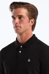 Polo de manga larga color negro, con cuello polo y tapeta de dos botones blancos. Presenta un pequeño logo bordado de pingüino en el pecho.