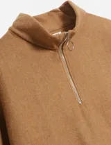 Poncho de color camel con cuello alto y cierre frontal parcial con tirador de anillo metálico. Presenta una textura suave y abrigada.