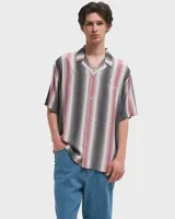 Camisa de manga corta con rayas verticales en tonos gris, rosa y blanco. Tiene cuello tipo cubano, cierre con botones y logo bordado en el pecho.