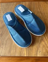 Pantuflas de tela acolchada color azul con suela blanca y etiqueta con el logo de la marca.