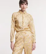 Camisa color dorado con estampado geométrico plateado, de manga larga con puños abotonados, cuello camisero y cierre frontal con botones ocultos.