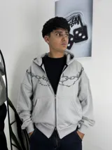 Campera con capucha y cierre frontal, de corte boxy y diseño holgado. Presenta un estampado gráfico de cadenas que recorre la parte superior del pecho y los hombros.