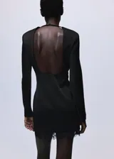 Vestido corto entallado de color negro, con cuello redondo y manga larga. Presenta un diseño de espalda abierta con tiras y un delicado detalle de encaje en el bajo. Incluye forro interior y cierre de cremallera en la parte posterior.