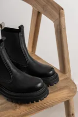 Botas tipo chelsea de cuero negro con textura granulada, paneles laterales elásticos y suela track robusta de goma.