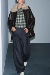 Chaqueta de efecto cuero color marrón oscuro con acabado brillante, cuello de solapa con aplicación de pelo sintético extraíble, manga larga con trabillas, bolsillos frontales de plastrón con solapa y cierre frontal con cremallera y botones a presión.