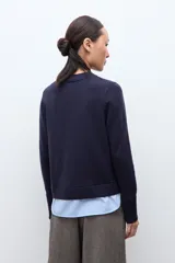 Sweater azul marino de manga larga con cuello redondo, combinado con una camisa celeste que se asoma por debajo.