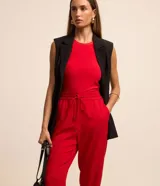 Pantalón de crepé rojo, modelo estilo pijama, de corte fluido, con cintura elástica y lazo de ajuste con terminales metálicas. Cuenta con bolsillos laterales y cierre frontal con cremallera y botón.