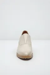 Zapato de cuero color beige, con taco de madera y suela dentada. Presenta un diseño slip-on con detalles de textura en relieve en los laterales y el empeine.