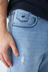 Jean de corte recto en color azul claro, con diseño de tiro medio y cintura regular. Presenta detalles de roturas en las rodillas y logo bordado en el bolsillo pequeño delantero.