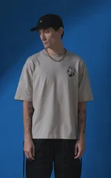 Remera de manga corta y cuello redondo con calce oversize, color beige con estampa gráfica en negro que incluye texto y un rostro femenino estilizado con llamas.