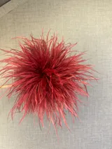 Broche decorativo confeccionado con plumas de avestruz en color rojo intenso, con forma circular y volumen.