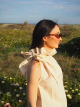 Blusa de lino sin mangas, con cuello alto fruncido y un lazo decorativo al costado. Diseño a rayas finas en tonos amarillo manteca y blanco, con corte recto y ligero.