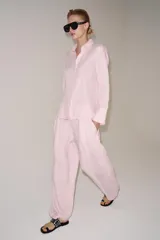 Pantalón de tiro medio confeccionado en 100% lino color rosado, con diseño de pernera ancha, pinzas en el delantero, cintura elástica en la parte posterior y bolsillos laterales. Cuenta con cierre frontal con cremallera y botón.