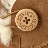 Botas cortas UGG color marrón claro, de gamuza con interior de piel de oveja. Presentan un botón de madera con el logo de la marca en el lateral.