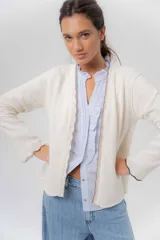 Saco básico de punto color marfil, confeccionado en lambswool, con corte entallado tipo chaquetita. Destaca por detalles de blonda tejida en los puños y a lo largo de la abertura frontal, con bordes en color contrastante.