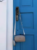 Bandolera compacta de cuero sintético con textura granulada, color beige. Incluye una correa ancha ajustable con un monedero circular desmontable y cierre superior con cremallera.