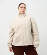 Campera deportiva de sherpa color beige, con cuello alto, cierre frontal completo y bolsillo con cierre en el pecho. Presenta un corte boxy holgado, mangas largas y acabado de textura suave.