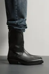 Bota estilo cowboy de color negro, con acabado liso, tiradores laterales, horma en punta, suela a tono y tacón ancho.