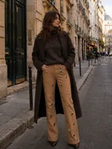 Jean de tiro alto color beige con diseño de ojalillos metálicos distribuidos por toda la prenda. Presenta un corte recto y holgado.