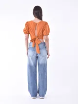 Blusa corta color naranja, con mangas abullonadas y puños elásticos. Presenta un diseño ajustado en la cintura y escote redondo.