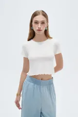 Remera crop de manga corta en tejido de poliamida al cuerpo, de color blanco, con cuello redondo y terminaciones con volados sutiles en mangas y ruedo.