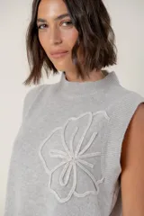 Chaleco de lana color crema con diseño de flor bordada en relieve en el frente, cuello redondo y aberturas laterales en el ruedo.