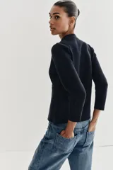 Chaqueta de punto color negro con cuello redondo, manga larga y cierre frontal con botones dorados. Presenta un corte entallado con bajo en evasé.