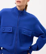 Campera de punto pesado color azul, con cuello alto, cierre frontal con cremallera y bolsillos delanteros con solapa y botones. Cuenta con mangas largas y puños y bajo acanalados.