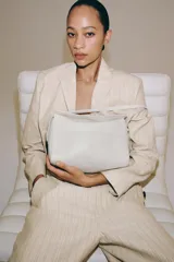 Bolso de hombro de piel en color blanco, con solapa, cierre de cremallera metálica, asa de hombro y bolsillos en el interior y exterior.