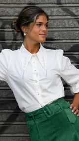 Camisa blanca de mangas largas con cuello con apliques de flores y perlas, y botones dorados.