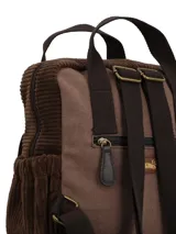Mochila de diseño patchwork en tonos marrones, confeccionada en textil con detalles de pana y gamuza. Presenta un bolsillo frontal con solapa, manijas superiores fijas, correas ajustables y un llavero decorativo con borlas y cuentas en el lateral.