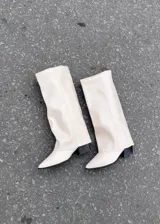 Botas altas de ecocuero color blanco hueso, con diseño slouchy de caña ancha y recta, punta fina y tacón cuadrado bajo de color negro.