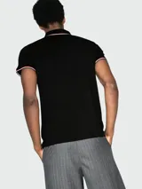 Polo de piqué de algodón blanco de manga corta, con cuello y puños con ribetes tricolor (rojo, blanco y azul marino). Presenta un pequeño logo bordado en el pecho.