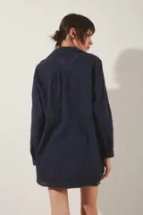 Camisa de corte amplio en color azul marino, con cuello clásico y cierre frontal de botones. Presenta delicados bordados florales tono sobre tono en el frente, mangas y espalda. Las mangas largas incluyen presillas internas para ajustar su largo.