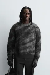 Jersey de corte relajado con cuello redondo y manga larga, confeccionado en tejido cepillado con patrón jacquard en tonos oscuros y acabados en rib.