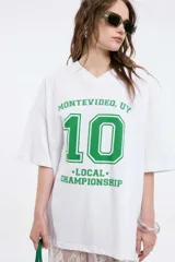 Remera oversize gris oscuro con cuello en V y mangas cortas. Presenta una estampa frontal estilo universitario con el número "09" y las inscripciones "MVD", "UY" y "PIMENTÓN ACTIVE" en tonos celestes y blancos.